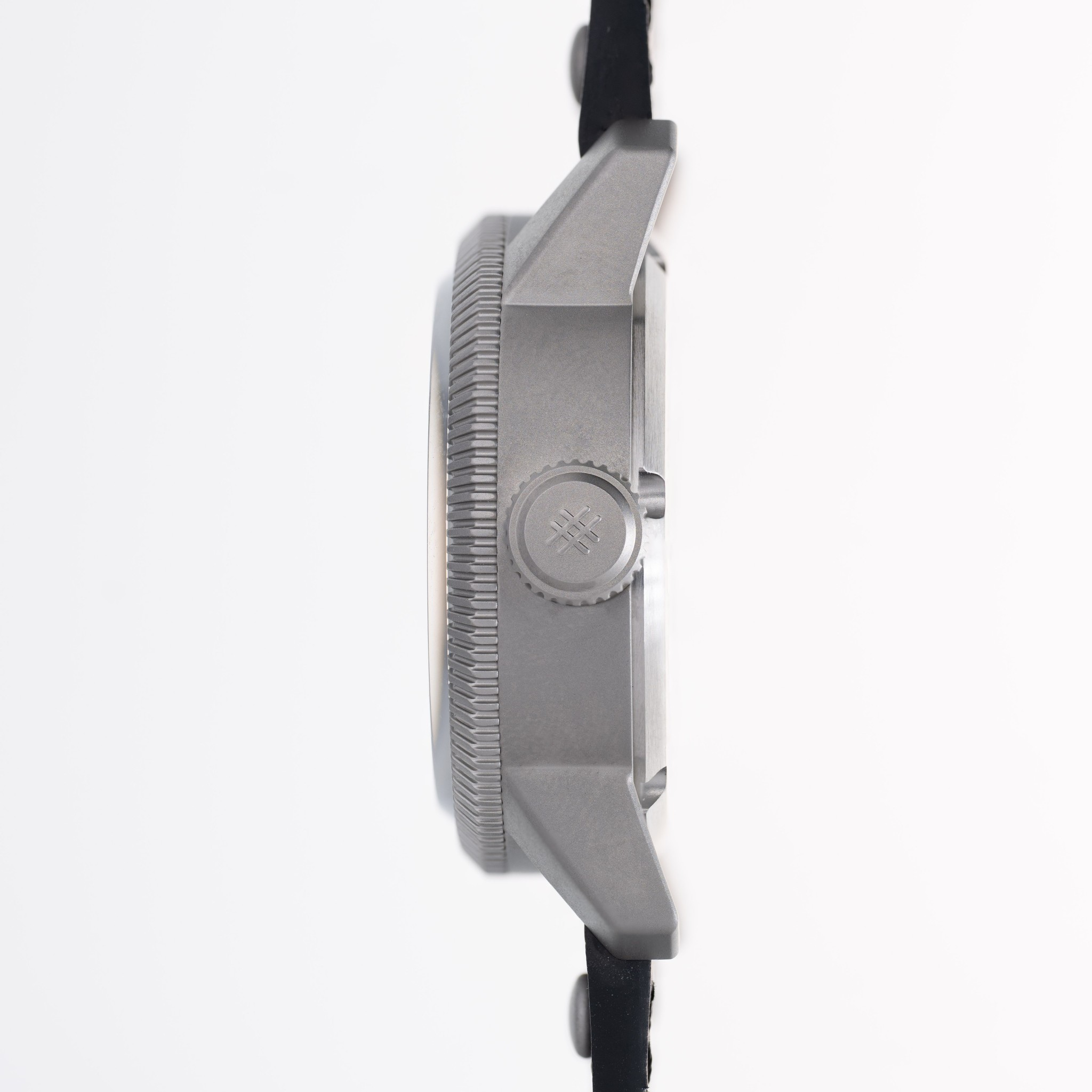 Side profile of a rugged stainless steel watch with a textured bezel, crown button, and black strap on a clean white background.